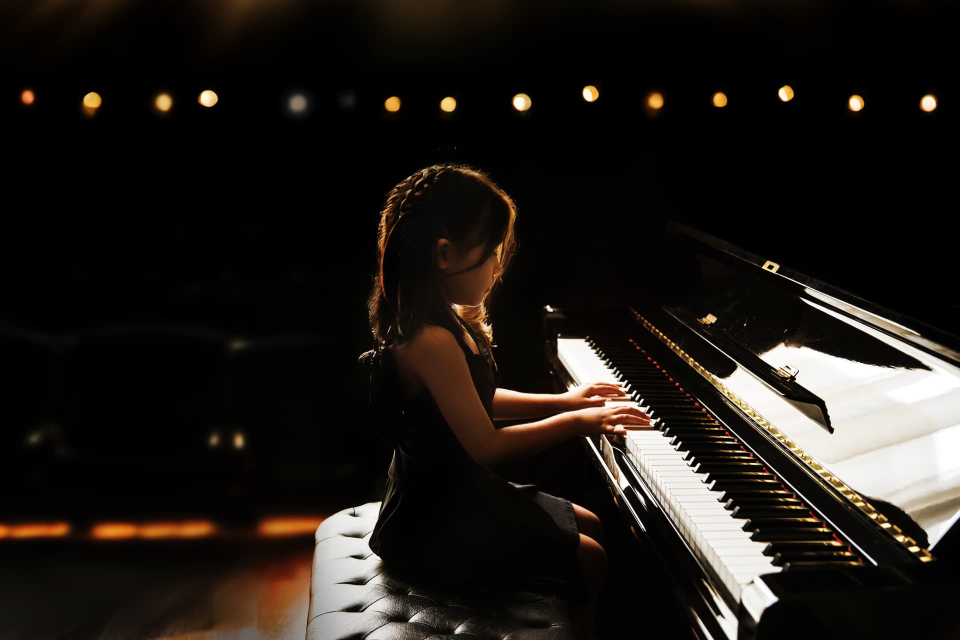 A young pianist performing on a grand piano under warm stage lights